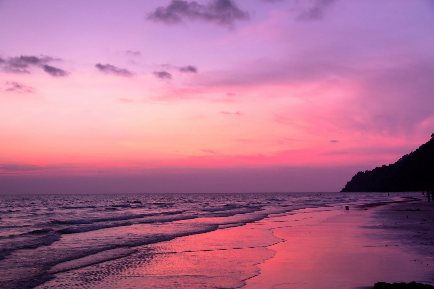 A sunset over a large beach with the sun illuminating the entire scene in a pink/orange colour.